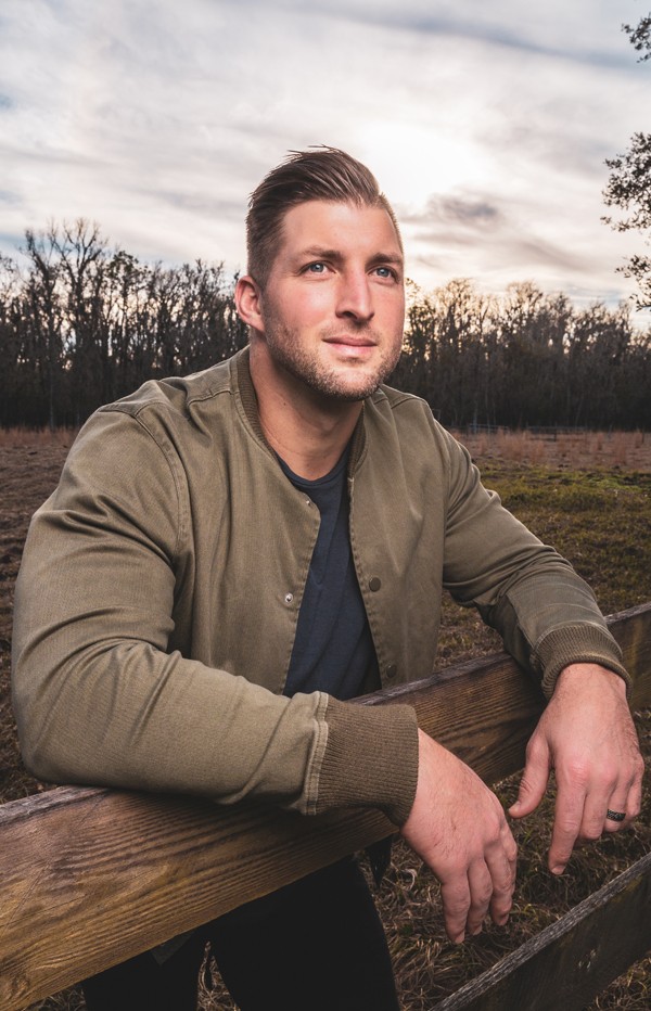 Tim Tebow's Mission Possible Video Curriculum About Tim Bio Photo Leaning Over Fence In a Field